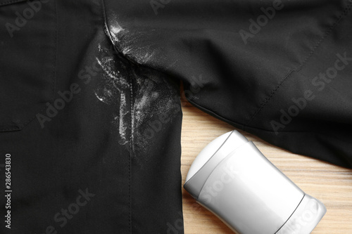 Black shirt with stain and deodorant on wooden background, closeup
