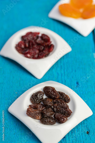 Dried raisins in small white saucers on a wooden blue background.