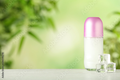 Deodorant container and ice cubes on white wooden table against blurred background. Space for text
