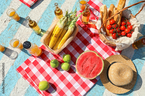 Straw hat and different products for summer picnic on checkered blanket, flat lay