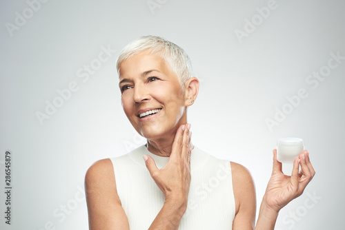 Gorgeous smiling Caucasian senior woman trying out new anti age cream. Beauty photography. photo