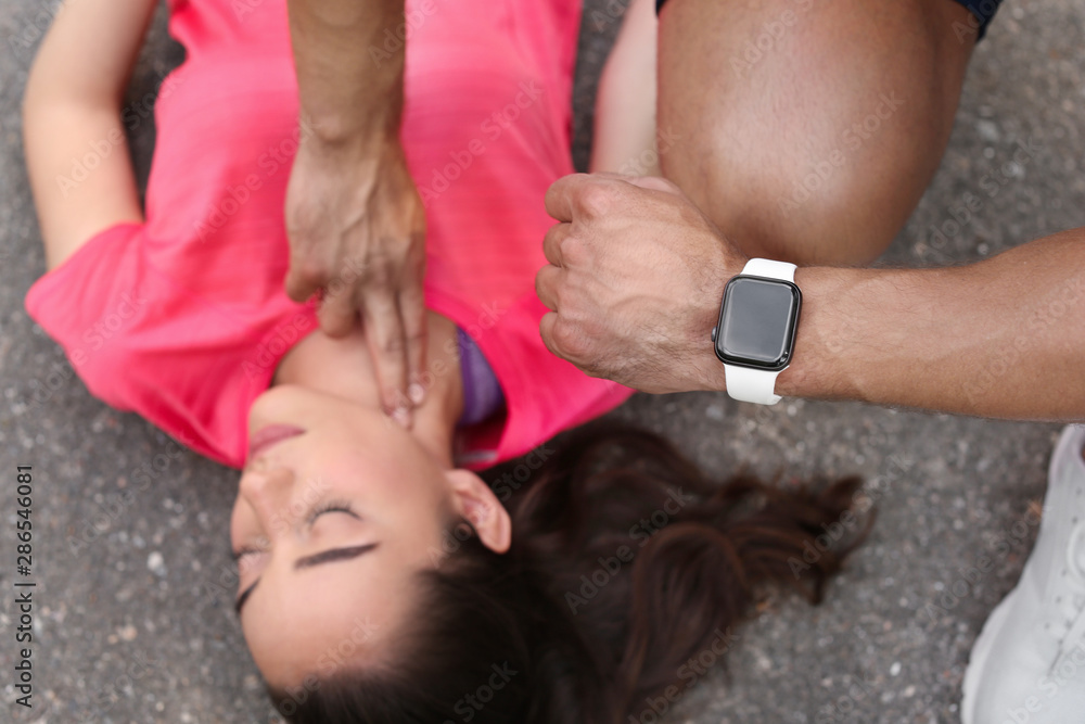 Fototapeta premium Young man checking pulse of unconscious woman on street