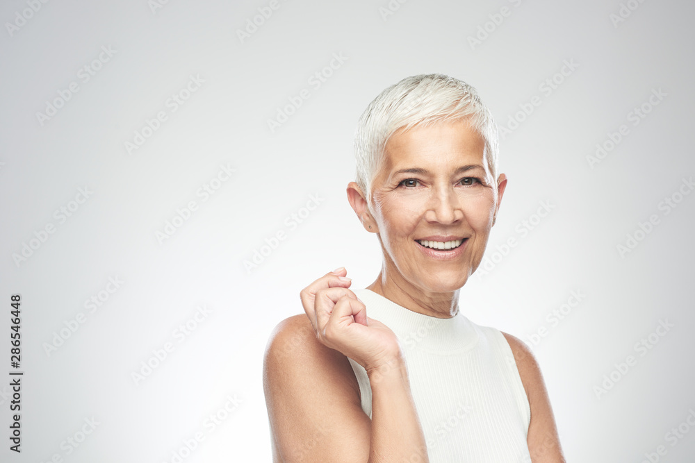 Beautiful smiling senior woman with short gray hair posing in front of gray background. Beauty photography. Beautiful smiling senior woman with short gray hair posing in front of gray background. Beauty photography.