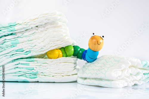 Toy worm with smile next to a pile of diapers, to illustrate concepts of health and childhood intestinal diseases. Isolated on white
