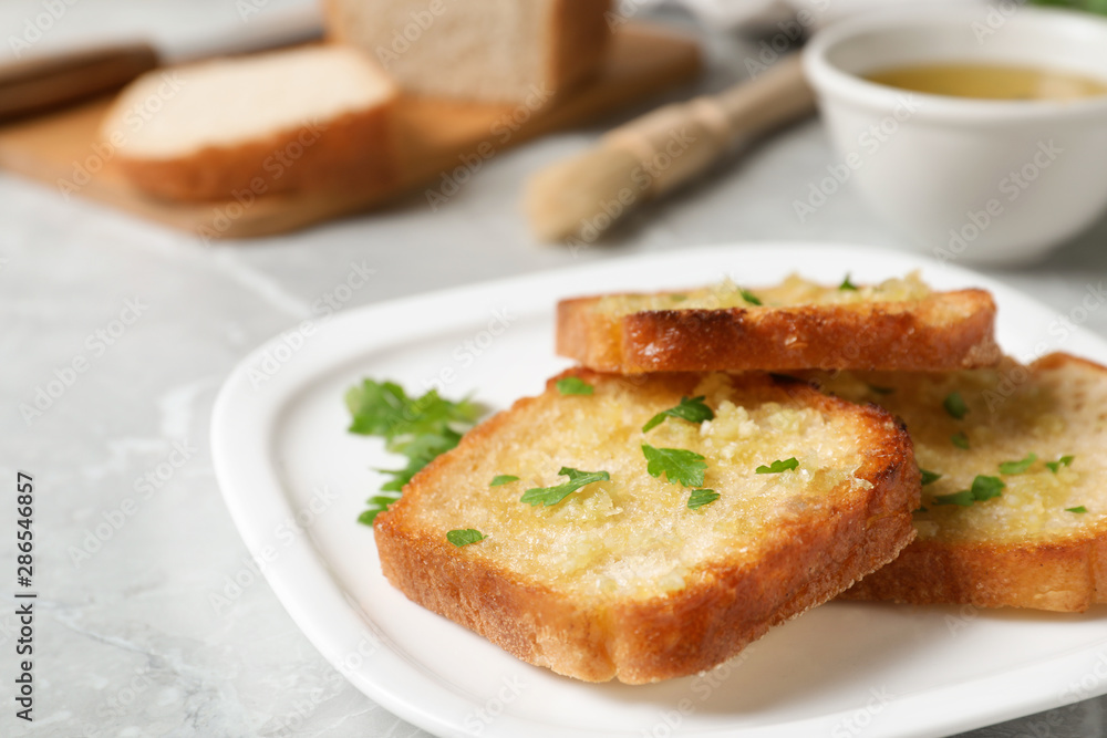 Slices of toasted bread with garlic and herb on light grey marble table, closeup