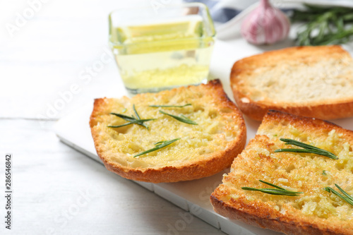 Slices of toasted bread with garlic and herb on white wooden table, closeup