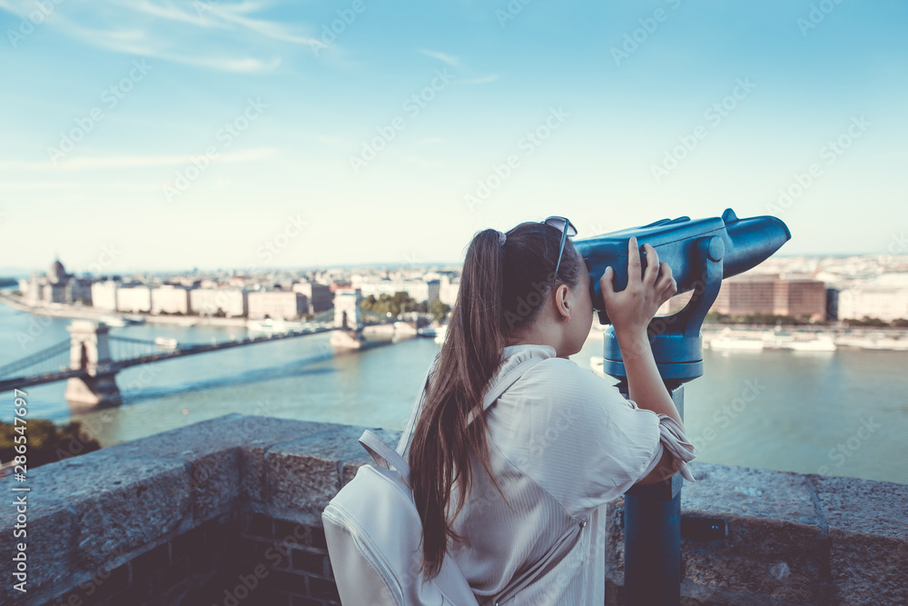 Pretty young brunette woman looking to historical city of Budapest by the big telescope, outlook, view to the city