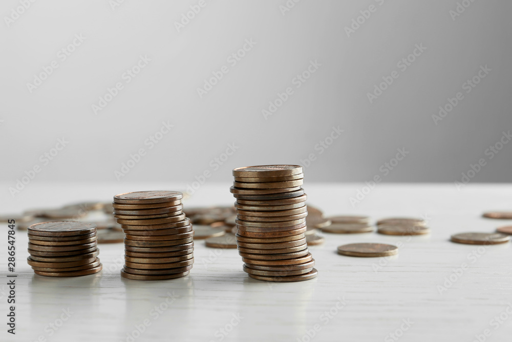 Stacked coins on white wooden table against light background Stacked coins on white wooden table against light background