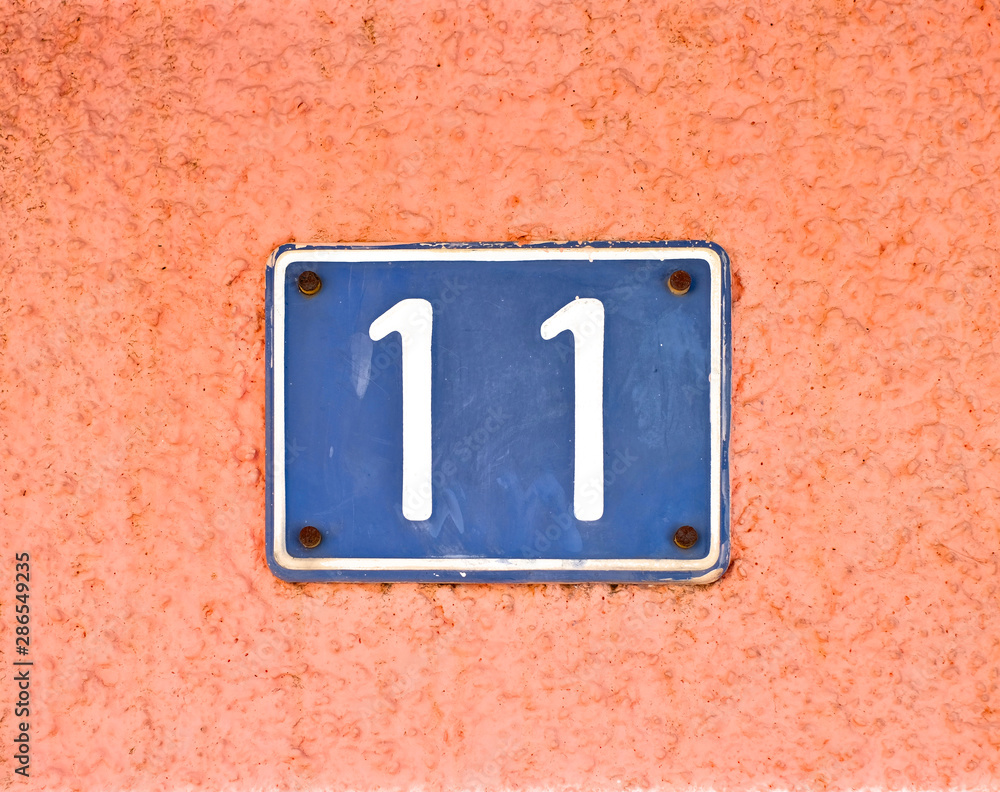 Number 11 / eleven, blue plate on pale pink wall surface. Number 11 / eleven, blue plate on pale pink wall surface.
