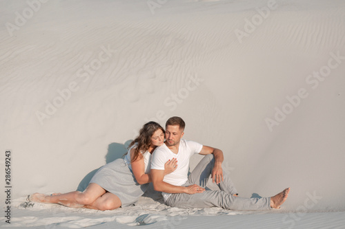 Romantic pair sit on white sand and huggins  in desert