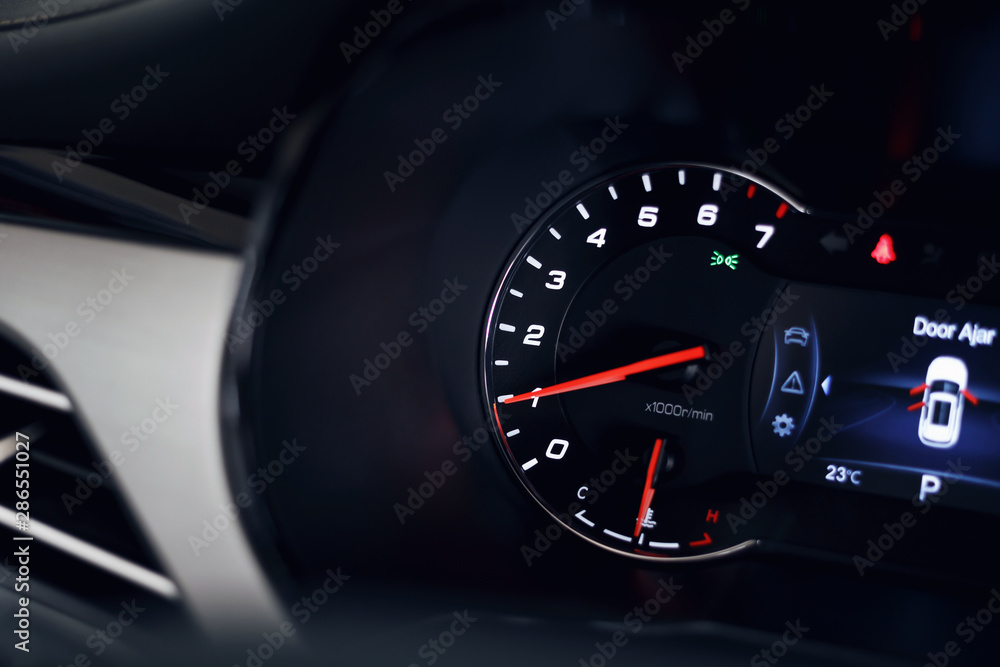 Close-up of the tachometer on the dashboard of a modern expensive car. The dashboard illumination is reflected. Front background is blurred