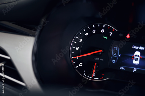 Close-up of the tachometer on the dashboard of a modern expensive car. The dashboard illumination is reflected. Front background is blurred
