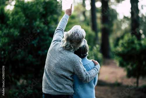 Couple of mature senior old people hug and enjoy the outdoor leisure activity together in the forest - green trees in background - unrecognizable man and woman for elderly healthy ilfestyle