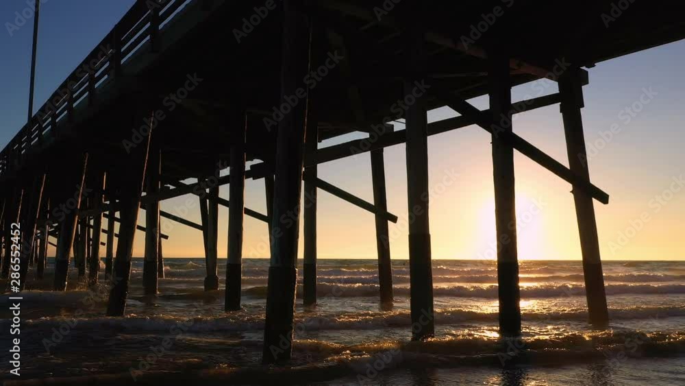 Aerial view under pier at Newport Beach as waves roll in as the sun begins to set. Aerial view under pier at Newport Beach as waves roll in as the sun begins to set.