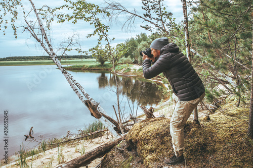 A man with a pick-up in a gray jacket, photographs nature on the banks of the river, in the forest