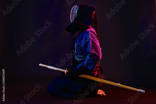 Close up shot, Kendo fighter wearing in an armor, traditional kimono, helmet practicing martial art with shinai bamboo sword, black background.