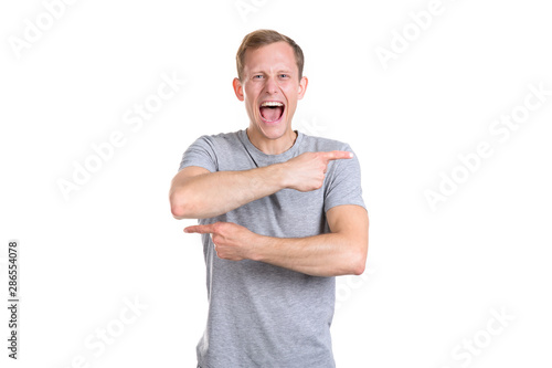 Young man in a gray t-shirt screams and points his fingers in different directions isolated on a white background. To doubt the direction - there or the court.