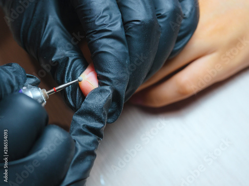 A master in nitrile gloves, uses an electric fingernail drill to remove rough skin from the middle finger. The process of removing rough skin from the middle finger.Hardware manicure