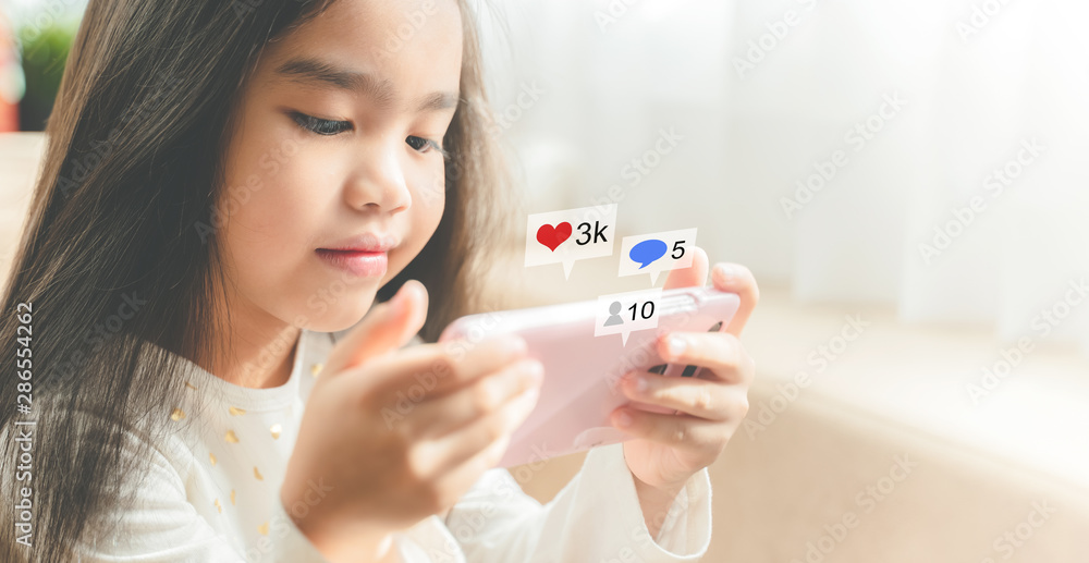 asian child using a smartphone and smiling while sitting on sofa at home, Hand using smartphone with Social media concept asian child using a smartphone and smiling while sitting on sofa at home, Hand using smartphone with Social media concept