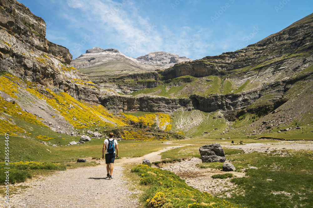 Hiker climbing on a trail path in a valley with cliffs and mountains on sides in the Pyrenees