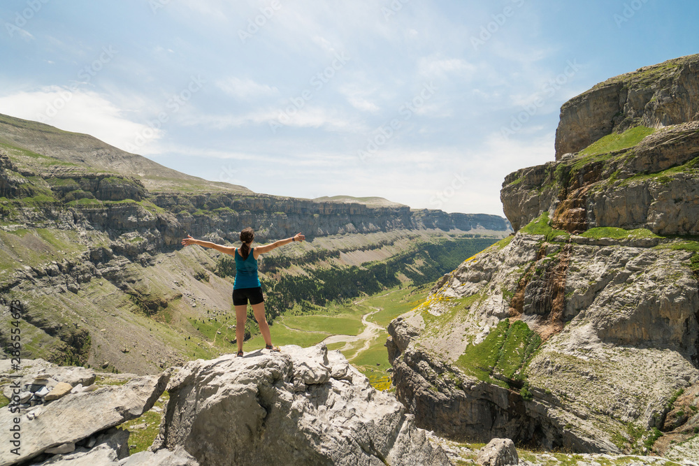 Backpacker hiker man on the top of a cliff in the mountains spreading arms and watching a beautiful view of the valley, in the Pyrenees