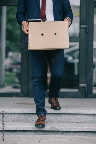 cropped view of dismissed businessman walking on stairs near building and holding box
