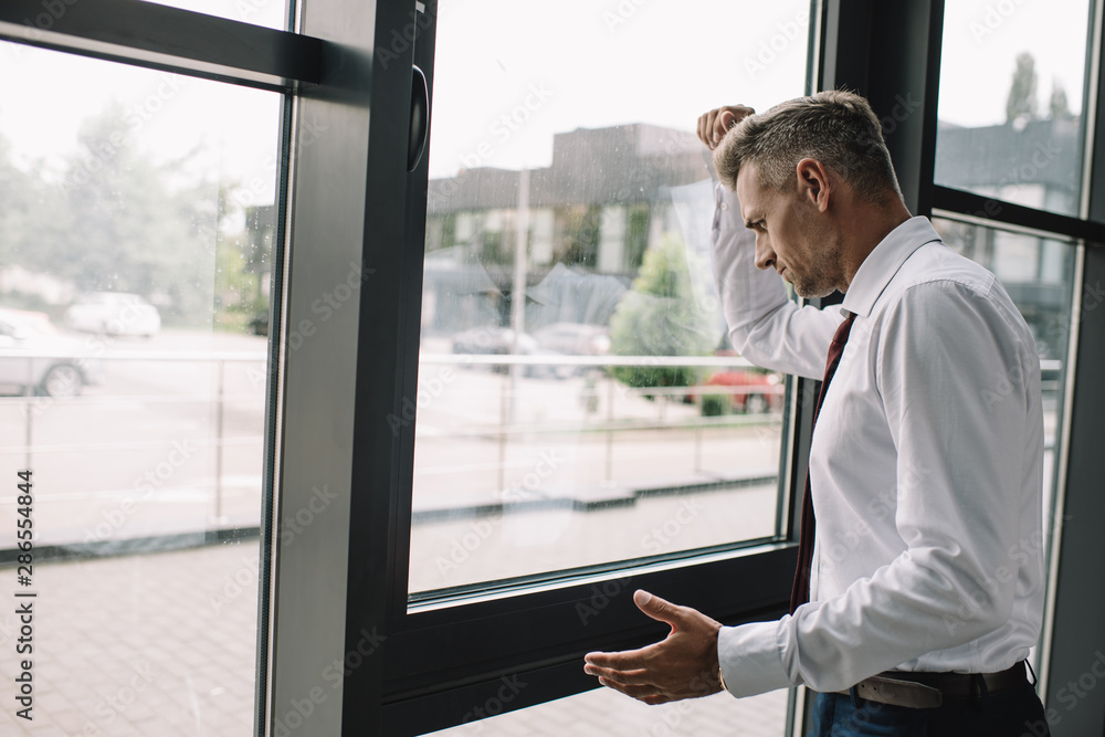 Fototapeta premium upset businessman standing with clenched fist near windows