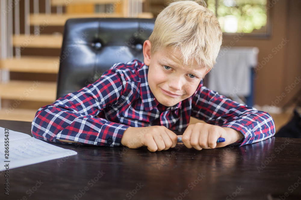 Sad schoolboy writing to notebook at home. Homework. Education, childhood and people concept