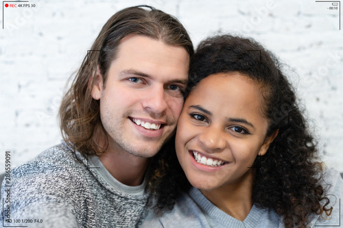 Portrait of young multiethnic couple make selfie recording video vlog from hands with mirrorless camera,  Volgging talking on live stream at white brick wall room. Concept Photographer live streaming. photo