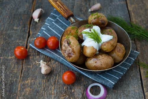 Fried potatoes with herbs and sour cream in a rustic style on a wooden table