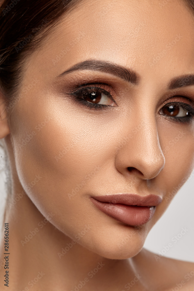 Close up portrait of a brunette nude model girl with professional evening make-up and plump lips, posing on gray background. Close up portrait of a brunette nude model girl with professional evening make-up and plump lips, posing on gray background.
