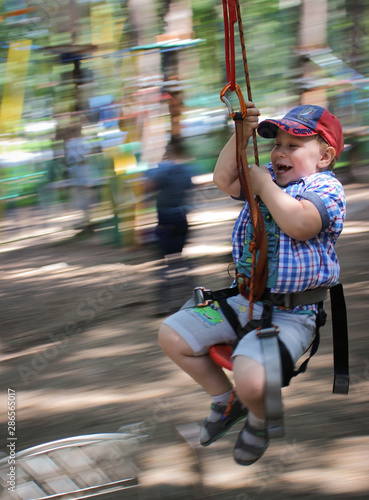 Young boy passing the cable route high among trees, extreme sport in adventure park.
