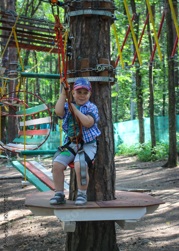 Young boy passing the cable route high among trees, extreme sport in adventure park.
