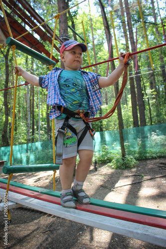 Young boy passing the cable route high among trees, extreme sport in adventure park.