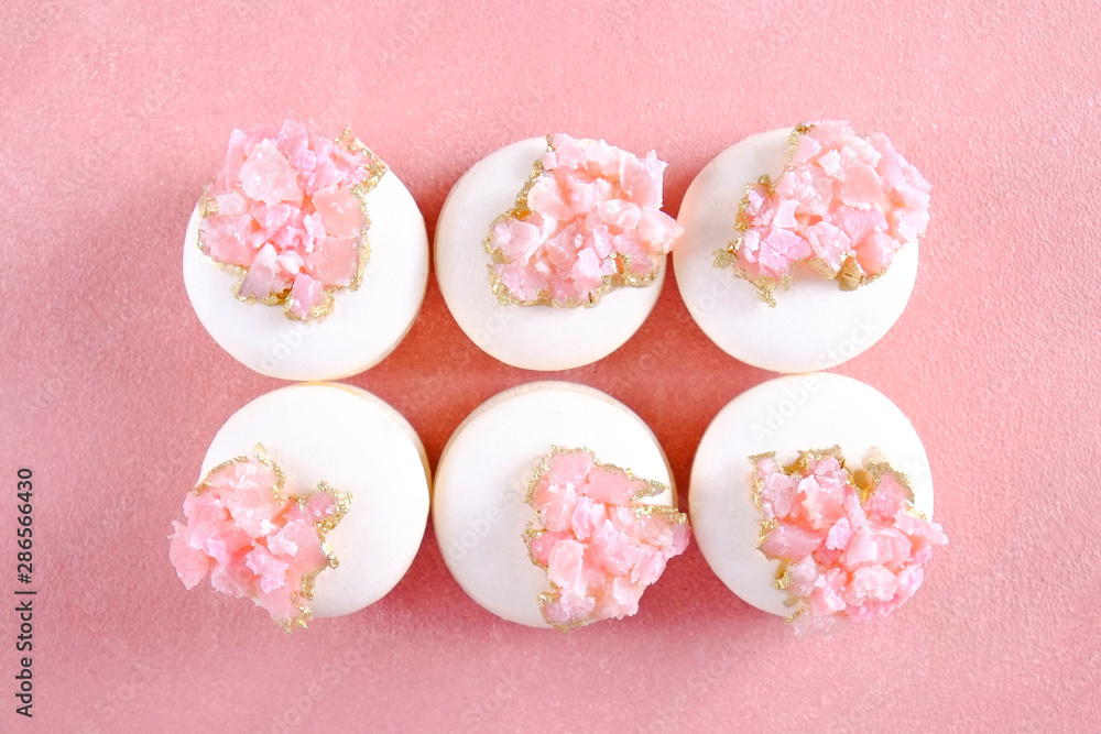 Minimalistic composition with bunch of white french macaron sweets with pink crystal shaped marmalade decoration over grunged concrete texture background. Top view, close up, flat lay, copy space.