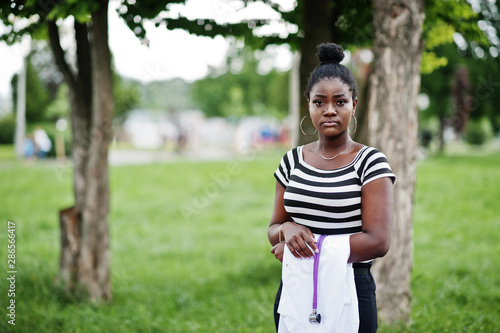 Young african american female doctor hold white coat on hand with a stethoscope posed outdoor.