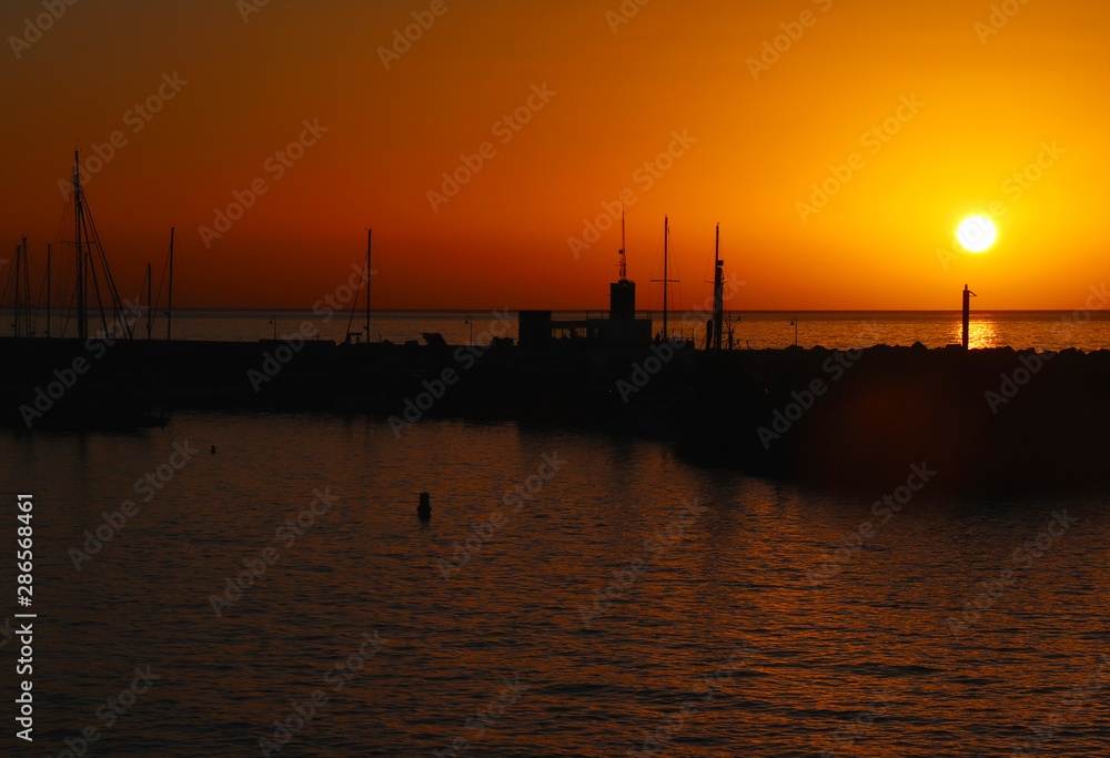 Boat and rock silhouette with orange and red sky and ocean water in Spain