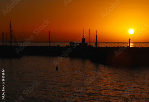 Boat and rock silhouette with orange and red sky and ocean water in Spain © Kari