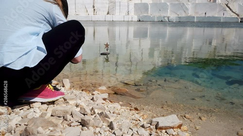 Young photographer woman playing with star boat toy on marble lake in Pamukkale, concept of lloneliness, depression, hope, love, success photo