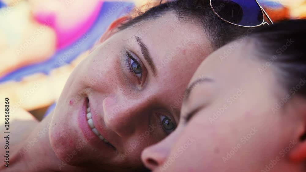 Closeup of two teen sleep on beach, open eyes and smile to camera Closeup of two teen sleep on beach, open eyes and smile to camera