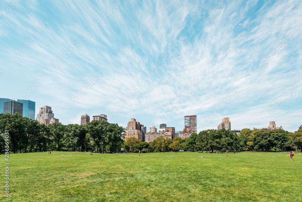 New York City/ Manhattan, NYC/ USA - 08 21 2017: Central Park on a sunny day with some clouds over the amazing skyline skyscraper of Manhattan CBD in Big Apple