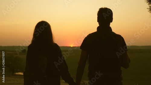 Travelers Man and woman raise their hands to sun and enjoy the sunset. Teamwork travelers with backpacks. Family of tourists on vacation. travels enjoy the scenery at sunset. Hiker Girl. Slow motion.