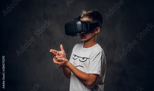 Young pretty schoolboy is playing virtual video game wearing special goggles.