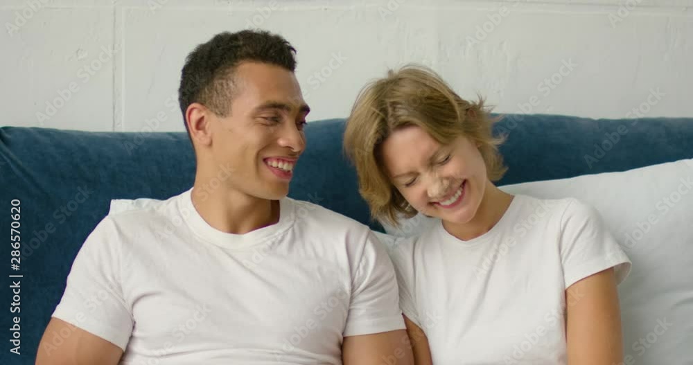 Young mixed race couple is relaxing in bed in the morning, both are talking, smiling, having nice time, enjoying their relationships, spending weekend at home. Hispanic, Caucasian. 4K, RED camera. Young mixed race couple is relaxing in bed in the morning, both are talking, smiling, having nice time, enjoying their relationships, spending weekend at home. Hispanic, Caucasian. 4K, RED camera.