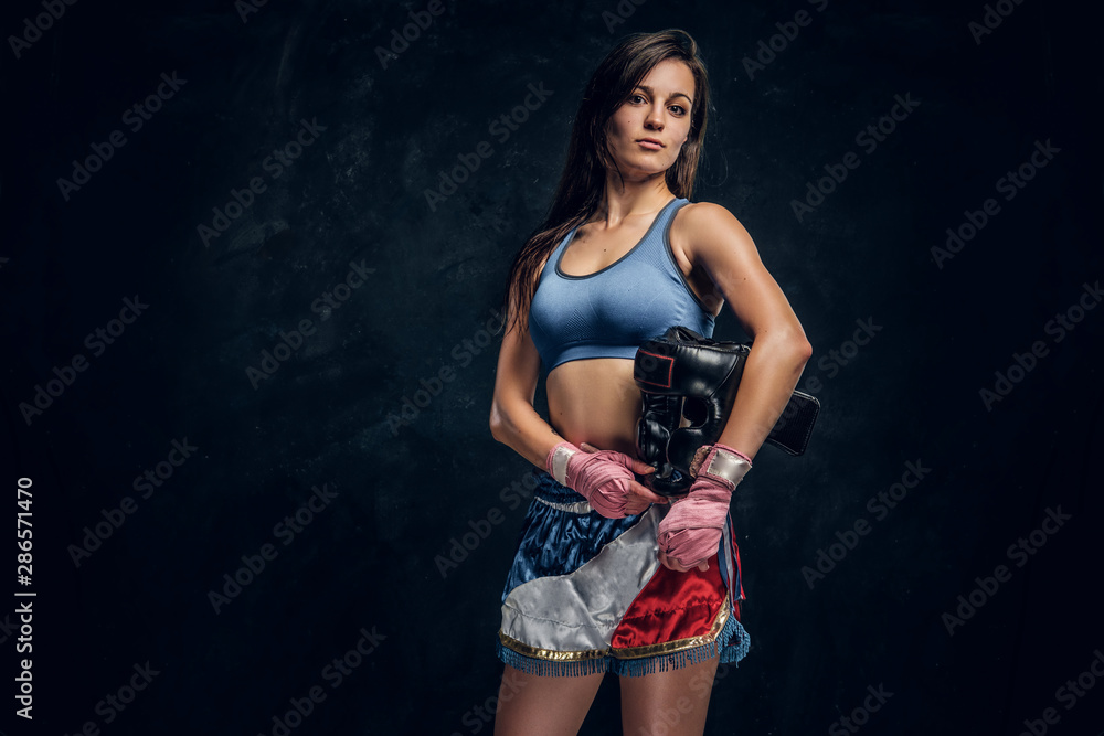 Portrait of young female boxer with her helmet in hands at dark photo studio.