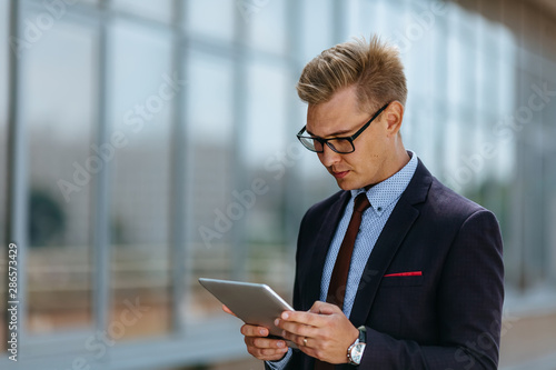 Elegant young businessman using his PC tablet. Portrait of a Male executive manager in trendy clothes with tablet pc in front of office building. Modern technology concept