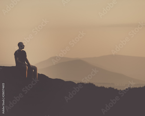 Young confident muscular male sat with a silhouette of mountains in the distance
