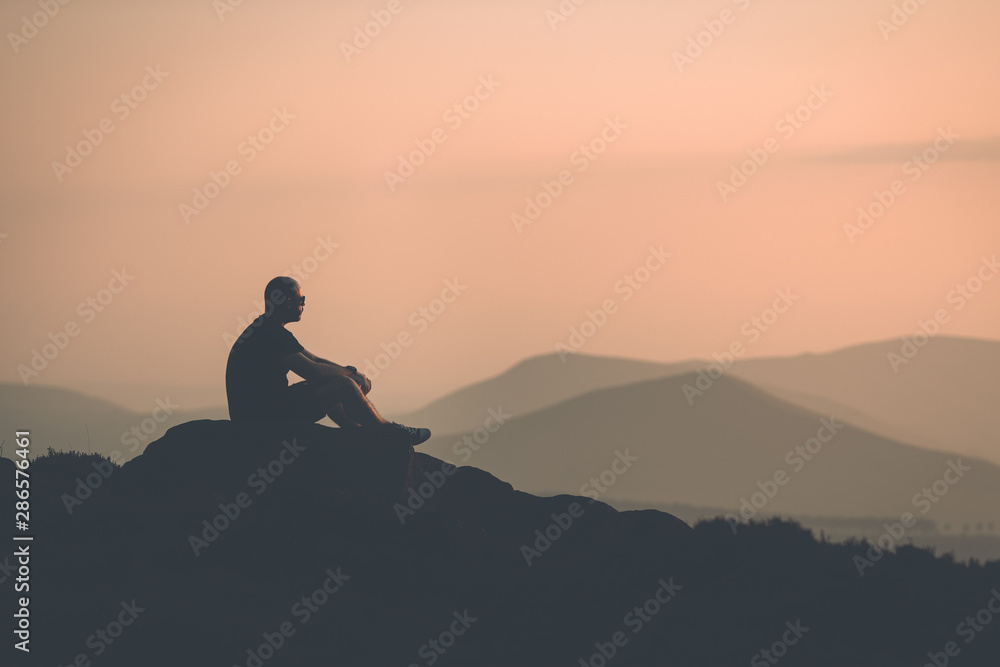 Young confident muscular male sat with a silhouette of mountains in the distance