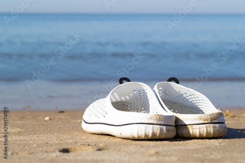 Holidays at sea. White sea slippers on the golden sand near the sea water. The best idea for a summer vacation.