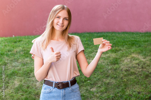 The girl showing thumbs up and holds in her hand a business card a mock up for the presentation of the design with copy space on a green background of nature
